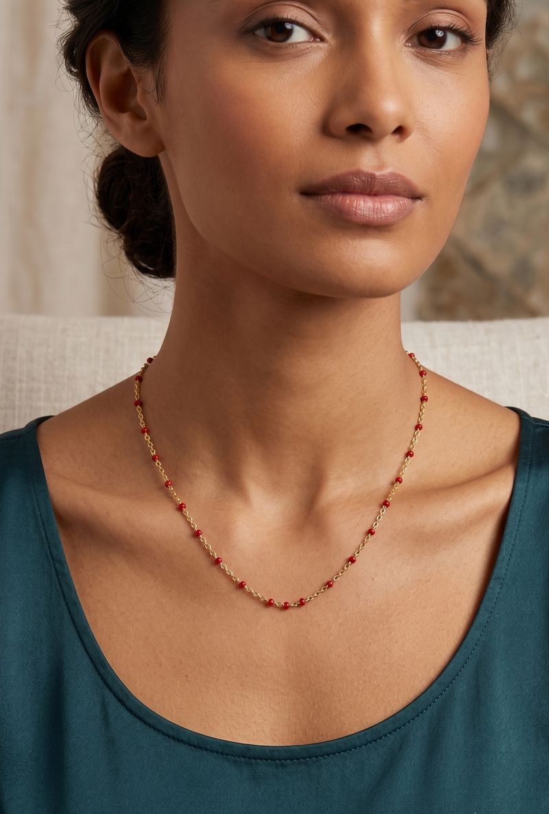 Model wearing gold red enamel bead station necklace with teal top